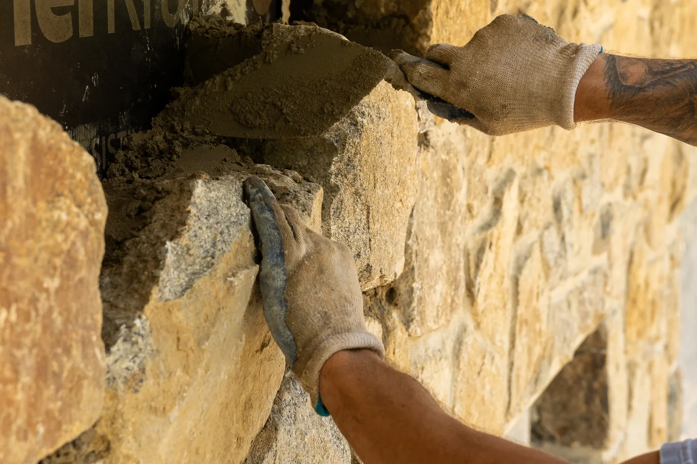 Gloved hands pointing mortar between stones